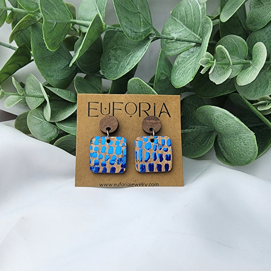 Cork over leather square earrings with round wood post. .75" squares with drops of metallic blue on natural cork.