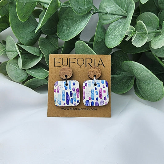 Cork over leather square earrings with round wood post. .75" squares with small watercolor brushstrokes in blue and purple over white.