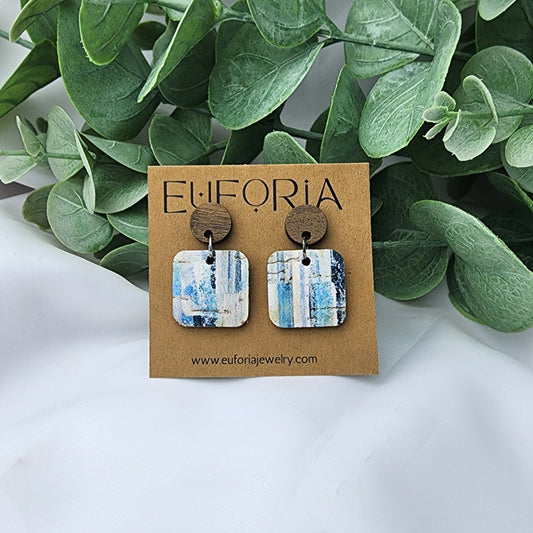 Cork over leather square earrings with round wood post. .75" squares with rustic style brush strokes in shades of blue over a white field.